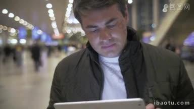 穿着夹克的年轻人在拥挤的机场使用平板电脑，方便使用便携设备工作